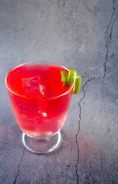 Üstünde limon dilimi olan bir bardak kırmızı içki. İçki, saplı uzun bir bardakta.