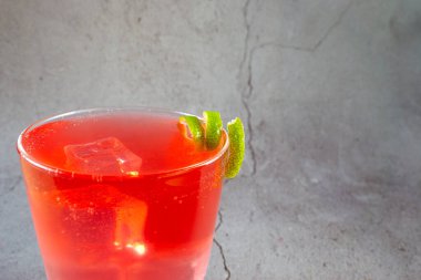 Üstünde limon dilimi olan bir bardak kırmızı içki. İçki uzun bir bardakta servis edilir ve limon bükülmesi sıvının üzerine konur. Rahatlama ve keyif kavramı