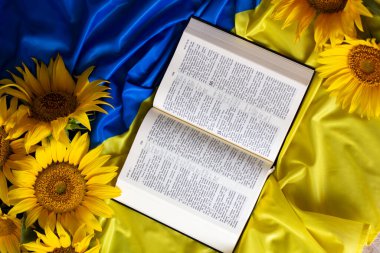 Bible (Holy Writ) and sunflowers on background of flag of Ukraine.