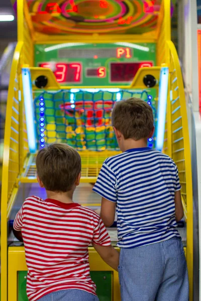 Entertainment center and children's area with slot machines. Two boys throws basketball in basket. Basketball arcade game.