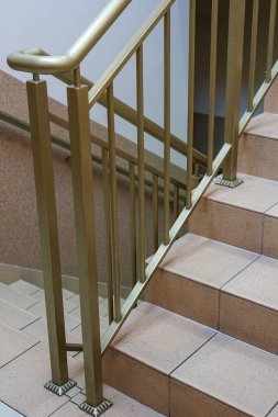 Kapalı bir merdiven, altın renkli metal korkuluk ve bej kaplamalı basamaklar.