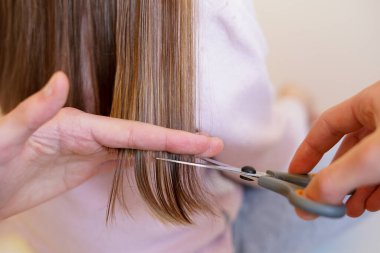 Saç kesimi sırasında uzun, düz kahverengi saçları makasla kesen bir elin yakın çekimi.