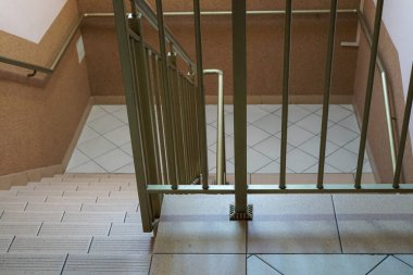 Kapalı bir merdiven manzarası, altın renkli metal korkuluklar ve bej kaplamalı zemin.