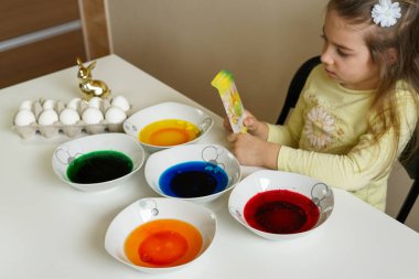 Küçük bir kız yumurtaları parlak boyalarla boyayarak Paskalya için hazırlanıyor.