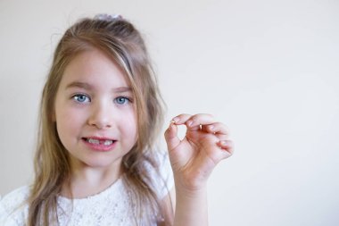 Genç bir kız, yakın zamanda kaybettiği bebek dişini dikkatlice inceleyip elinde tutuyor.