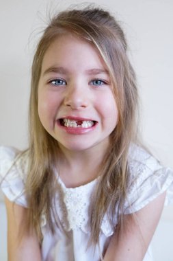 Beyaz bir elbise içinde gülümseyen, bebek dişleri eksik neşeli bir genç kız.