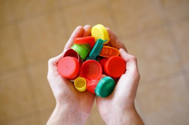 Plastik kapaklı ellerin yakın çekimi, geri dönüşümü ve çevre bilincini sembolize ediyor
