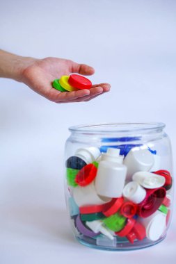 Geri dönüşüm ya da yeniden kullanım için plastik kapak dolu kavanozun üzerinde renkli kapaklar tutan kişi