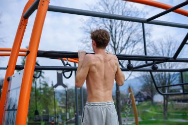 Genç adam üst vücut gücünü açık hava fitness binasında barfiks çekerek geliştiriyor.