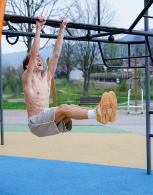 Atletik adam oyun parkında sallanan bacakları kaldırıyor.