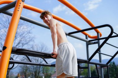 Genç adam barlarda antrenman yapıyor, mavi gökyüzünün altında sokak çalışması yapıyor.