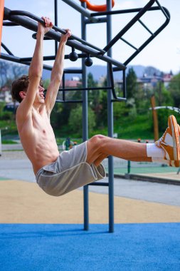 Atletik adam, açık hava fitness barında sallanan bacağını kaldırıyor.