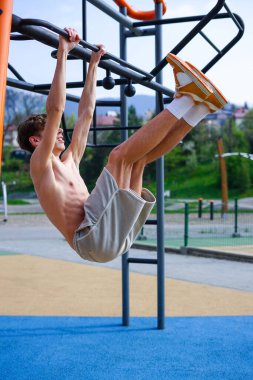 Genç adam güneşli bir günde parkta egzersiz istasyonunda bacak kaldırıyor..