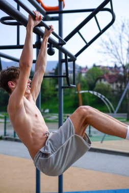 Atletik adam, açık hava fitness barında sallanan bacağını kaldırıyor.