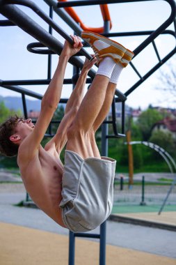 Genç adam güneşli bir günde parkta egzersiz istasyonunda bacak kaldırıyor..