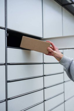 Paketi açık bir paket teslimat istasyonunun dolabına yerleştiren kişinin yakın plan fotoğrafı.