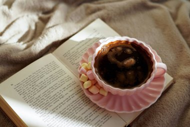 Bir fincan sıcak kahvenin, güzel bir kitabın ve huzurlu bir ortamda yumuşak marşmelovun tadını çıkar.