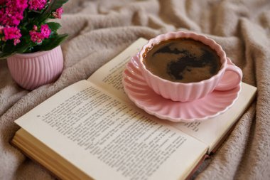 Açık bir kitabın üzerinde bir fincan sıcak kahve, huzurlu ve samimi bir atmosfer yaratıyor.