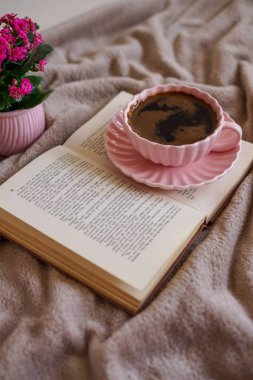 Açık bir kitabın üzerinde bir fincan sıcak kahve, huzurlu ve samimi bir atmosfer yaratıyor.