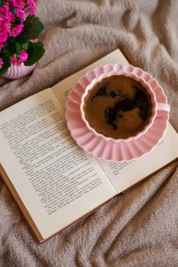 Açık bir kitabın üzerinde bir fincan sıcak kahve, huzurlu ve samimi bir atmosfer yaratıyor.