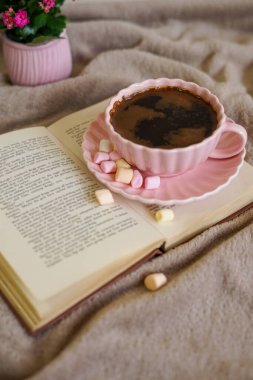 Renkli şekerlemeli sıcak bir fincan kahve, bir kitap ve mükemmel bir sıcak an için yumuşak bir battaniye.
