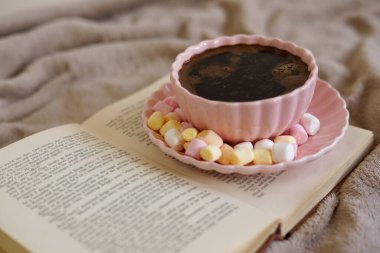 Renkli şekerlemeli sıcak bir fincan kahve, bir kitap ve mükemmel bir sıcak an için yumuşak bir battaniye.