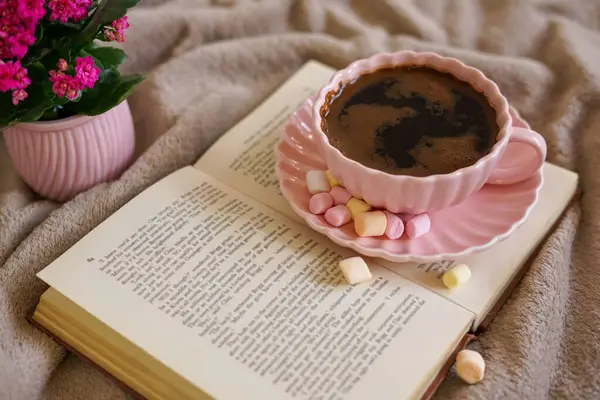 Renkli şekerlemeli sıcak bir fincan kahve, bir kitap ve mükemmel bir sıcak an için yumuşak bir battaniye.