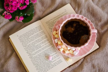 Renkli şekerlemeli sıcak bir fincan kahve, bir kitap ve mükemmel bir sıcak an için yumuşak bir battaniye.