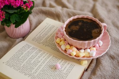 Renkli şekerlemeli sıcak bir fincan kahve, bir kitap ve mükemmel bir sıcak an için yumuşak bir battaniye.
