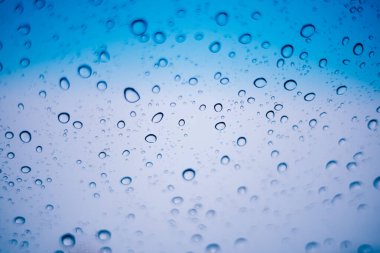 Blue water droplets and raindrops cling to the cool clear glass
