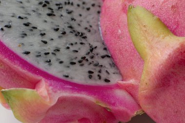 Pitahaya - ejderha meyvesi, ikiye bölünmüş, güzelliğini gösteriyor, detaylarla dolu, pembe ve yeşil deri ve tohumlu beyaz posa.
