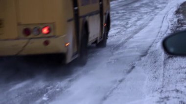 Yavaş hareket eden bir otobüsün tekerlekleri kar dalgalarını yükseltiyor asfaltta sürükleniyor, ilk kar.