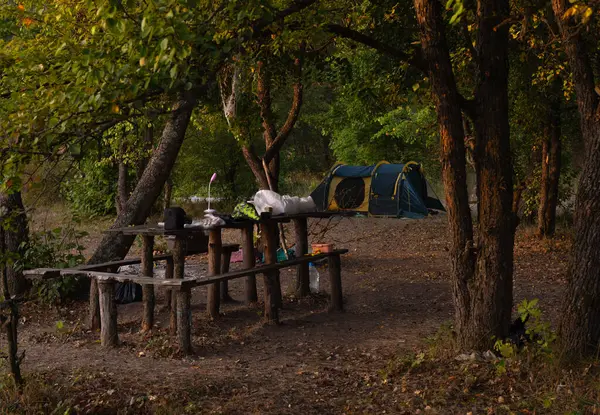 piknik, dinlenme yeri ahşap masa ve ağaçların arasında insanlar olmayan banklar, arka planda çadır.