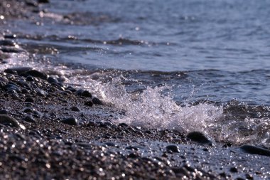 soft foamy waves roll on a pebble sea beach on a sunny hot day
