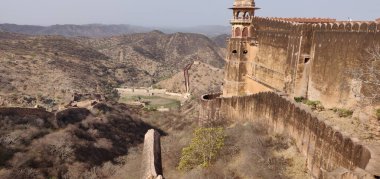 Uzakta bir kale ve önünde bir duvar görülür. Kale yemyeşil bir araziyle çevrili.