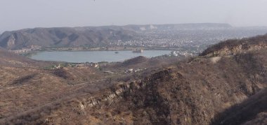 Ortasında göl olan bir dağ sırası. Göl engebeli arazi ve şehir binalarıyla çevrilidir. Huzurlu ve huzurlu bir sahne.