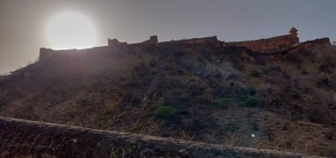 Uzakta şatosu olan bir yamaç. Güneş tepede parlıyor. Kale arka planda.