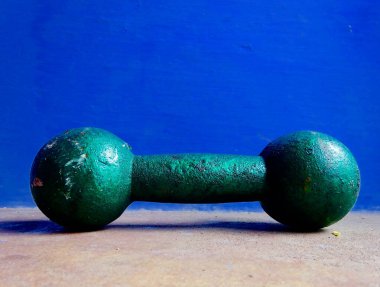 Kaba yeşil halterli, dokulu, parlak mavi arka planlı, zindelik, kuvvet ve retro antreman estetiği gösteren bir yüzey. Sağlık ve spor salonu ile ilgili kavramlar için ideal.