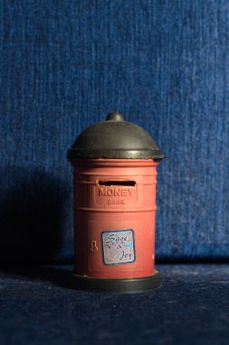 Vintage red cylindrical money bank with 'Save & Joy' label, resembling a postbox, set against a textured blue background, ideal for themes of savings, nostalgia, and financial planning. clipart