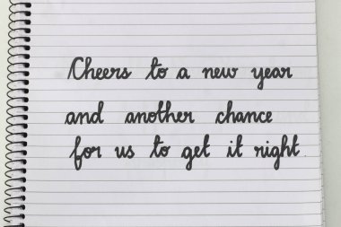 Handwritten inspirational quote in calligraphy: 'Cheers to a new year and another chance for us to get it right.' Black ink on lined notebook paper, spiral-bound. Perfect for New Year themes. clipart