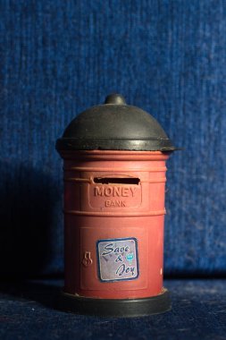 Close-up of a vintage-style red coin bank resembling a classic mailbox, labeled 'Money Bank' and 'Save & Joy,' set against a textured blue background. Perfect for retro, savings, and childhood themes. clipart