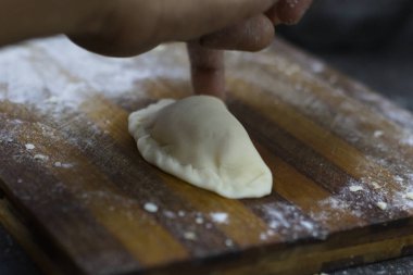 Ev yapımı hamur köftesini ahşap bir tahtaya koyup, etrafa saçılmış un saçarak, kırsal bir mutfak ortamında geleneksel pişirme hazırlıklarını sergiliyorlar..