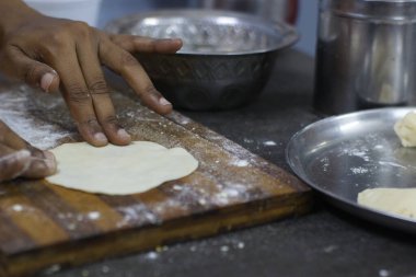 Mutfak aletleri ve unlarla çevrili ahşap bir kesme tahtasının üzerinde hamur hazırlayan elleri yakın plan. Gıda hazırlama, yemek pişirme veya mutfak temalı projeler için ideal.