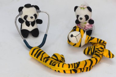 Playful plush toy setup: panda doctor with stethoscope examines tiger scarf, accompanied by a panda in a pink dress. Fun, imaginative, and whimsical scene perfect for children or creative storytelling. clipart