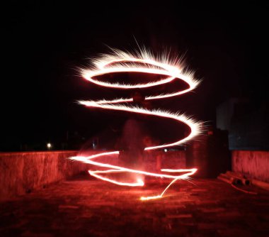 Dynamic light painting in a spiral pattern against a dark rooftop background, creating a mesmerizing long-exposure effect. Perfect for themes of creativity, energy, and celebration. clipart