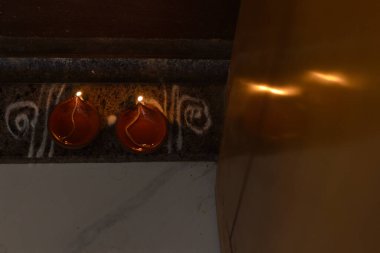 Parlayan alevlerle geleneksel kil gaz lambaları, beyaz Kolam sanat kalıplarıyla dekoratif taş bir yüzeye kurulmuş, dingin ve kültürel bir ortam yaratıyor..