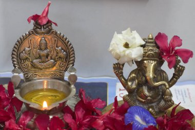 Traditional Indian brass decor: Lakshmi diya with burning oil lamp, Ganesha idol adorned with fresh flowers. Vibrant cultural elements for spiritual or festive themes. Ideal for editorial or decorative use. clipart