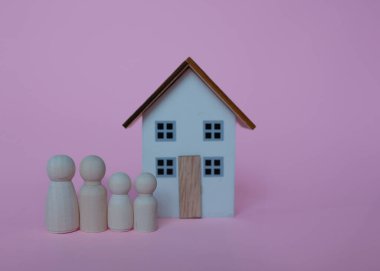 Bir çift ve bir çocuk heykeli ve pembe arka planda bir oyuncak ev.