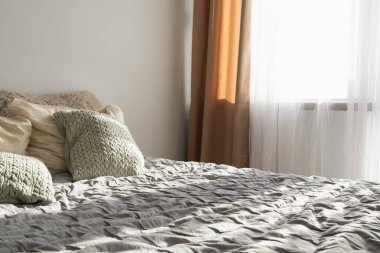  Yumuşak bir sabah ışığında rahat bir yatak odası. Dekoratif yastıkları ve battaniyesi olan bir yatak perdelerin arasından süzülen güneş ışığı sıcak bir atmosfer yaratır. Rahatlık ve rahatlama kavramları için mükemmel.