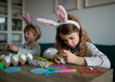 Sevimli küçük kız ve tavşan kulaklı şirin oğlan Paskalya için yumurta boyuyorlar.
